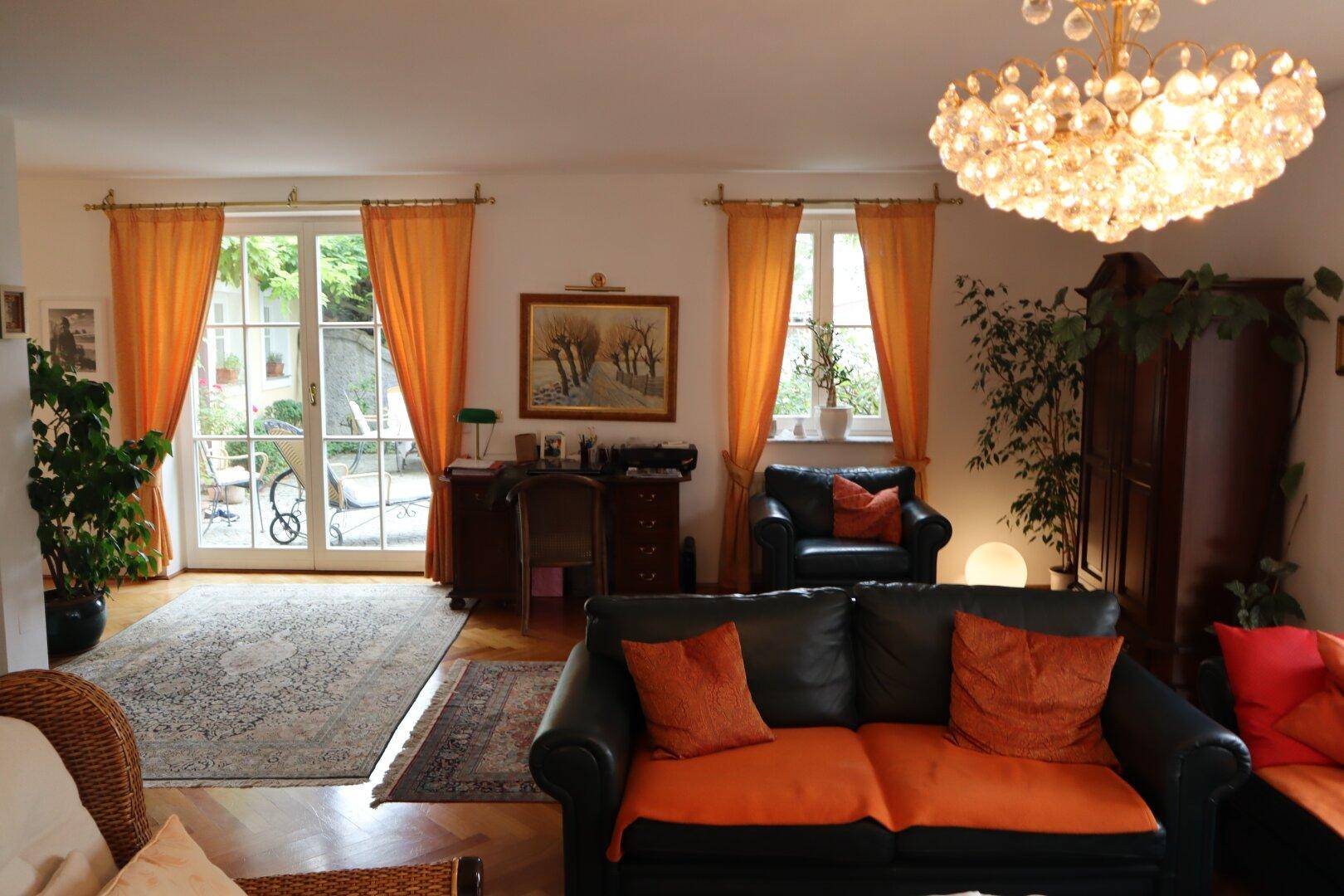 Geräumiges Wohnzimmer mit Parkettboden, großen Fenstern und Zugang zum Außenbereich.