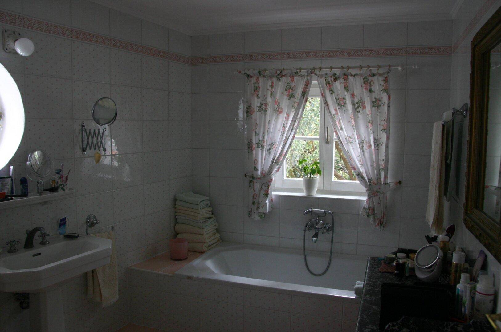 Gefliestes Badezimmer mit Waschbecken, Badewanne und Fenster für natürliches Licht.