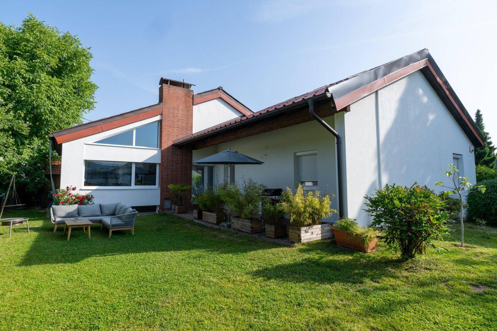 Seitliche Ansicht des Hauses mit großer Rasenfläche und einer modernen Lounge-Sitzgruppe im Garten.