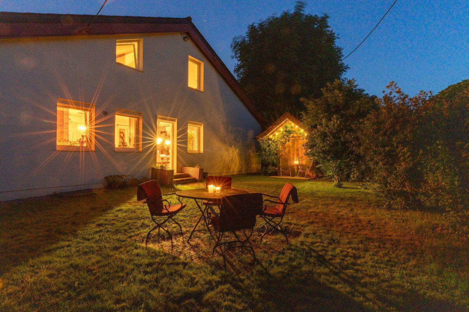 Abendliche Ansicht des Gartens mit beleuchteter Sitzgruppe und Gartenhaus, schafft eine gemütliche Atmosphäre.