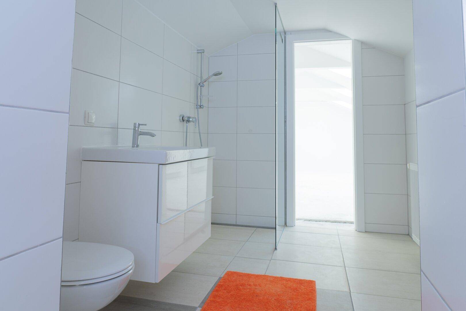 Modernes Badezimmer im Dachgeschoss mit weißen Fliesen, Waschtisch und bodengleicher Dusche.