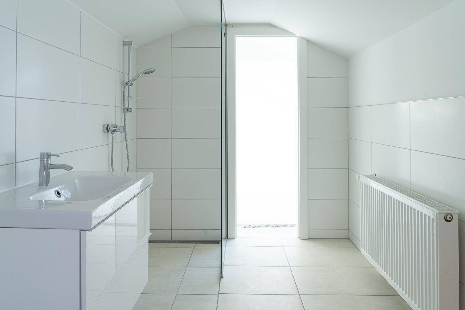 Helles Badezimmer im Dachgeschoss mit weißen Fliesen, modernem Waschtisch und Heizkörper.
