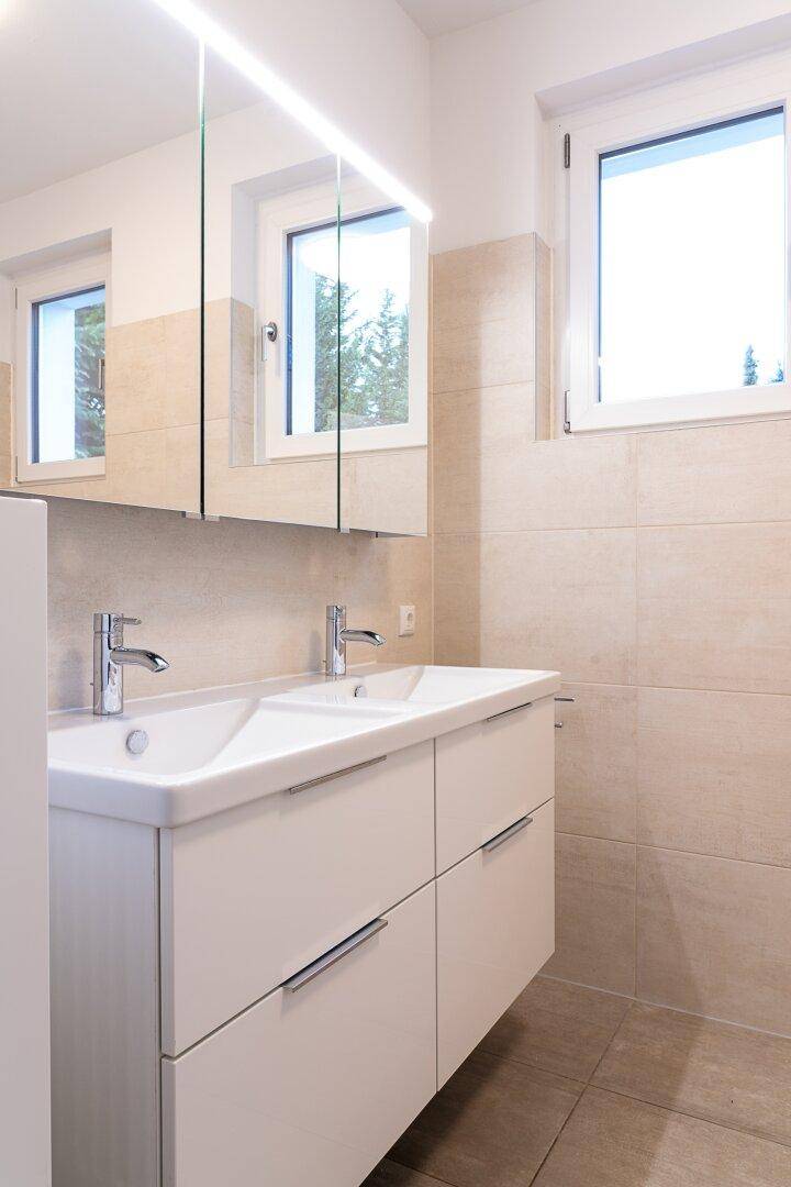 Modernes Badezimmer mit Doppelwaschbecken, Spiegelschrank und zwei Fenstern für Tageslicht.