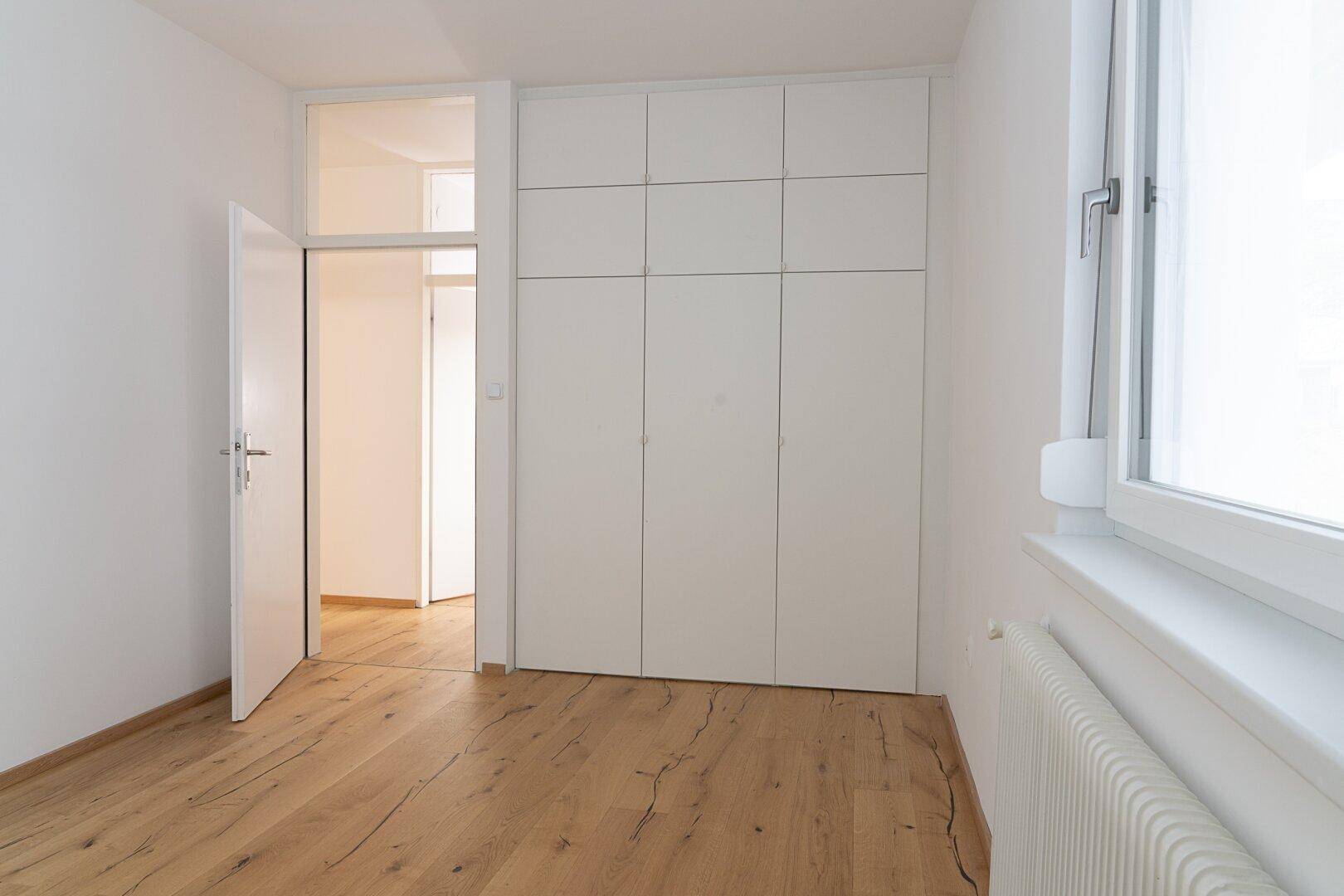 Helles Schlafzimmer mit Holzdielenboden und integriertem weißen Kleiderschrank, bietet viel Platz.