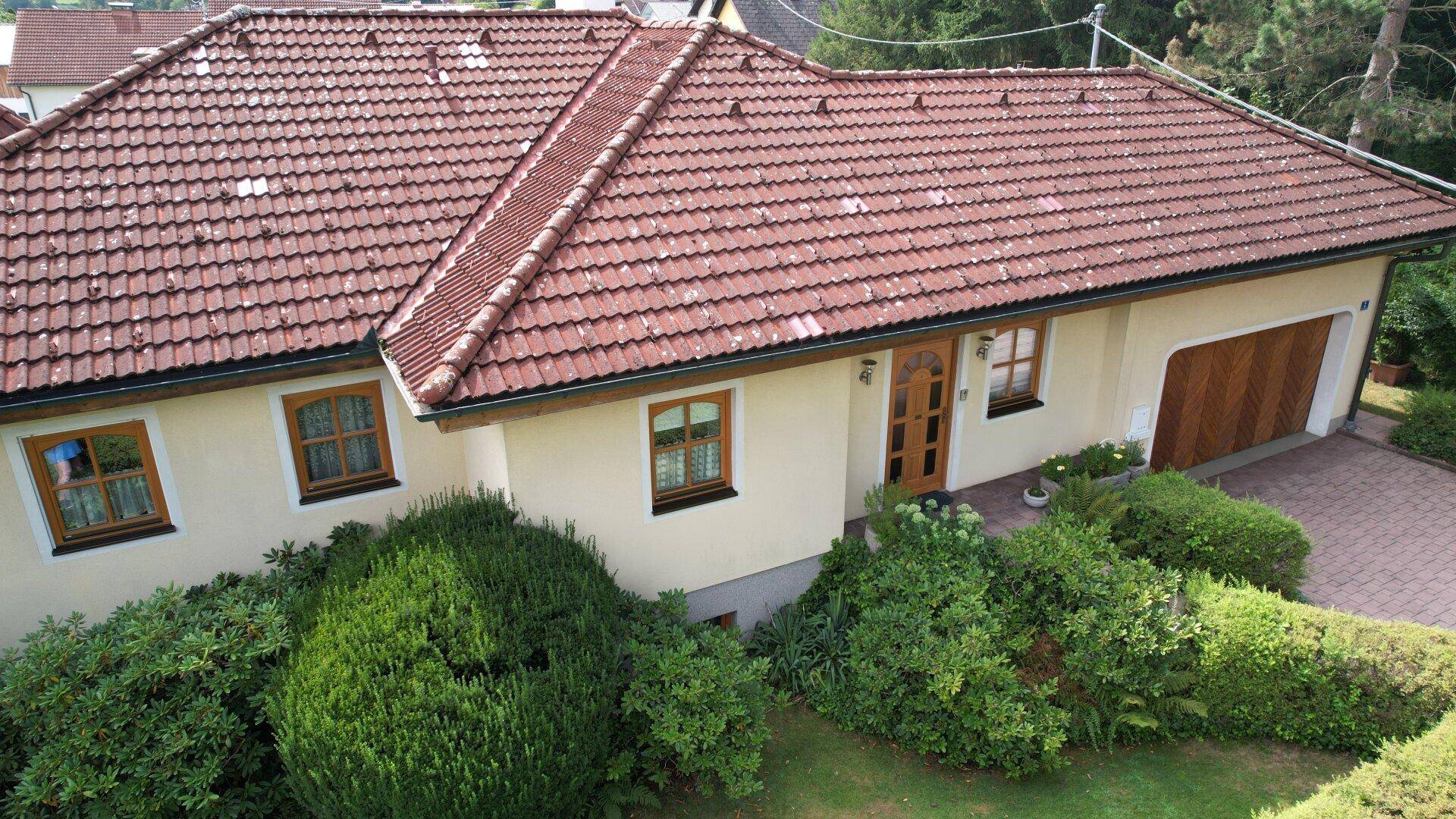 Seitenansicht des Hauses mit traditionellem Ziegeldach, Holzfenstern und integrierter Garage.