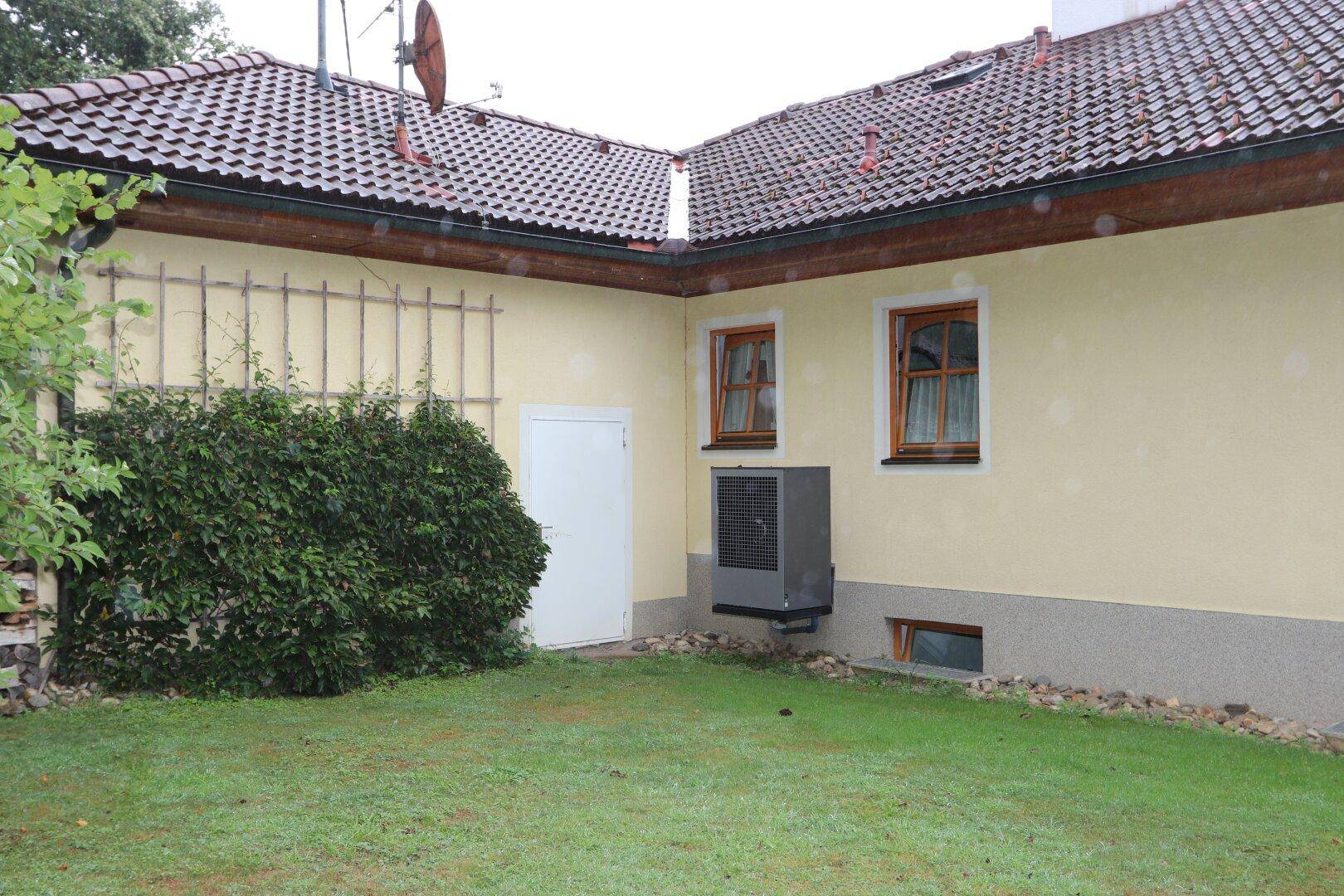 Rückseite des Hauses mit Wärmepumpe, kleinem Rasenbereich und Rankgitter an der Wand.