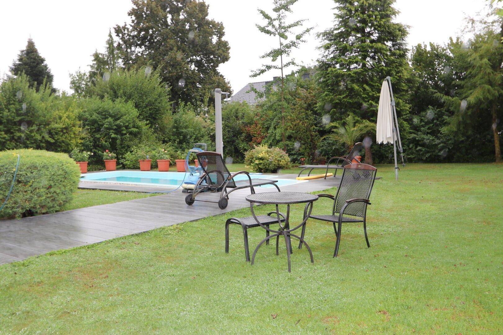 Weitläufiger Gartenbereich mit Pool, Liegestühlen und einem kleinen Tisch für entspannte Stunden.