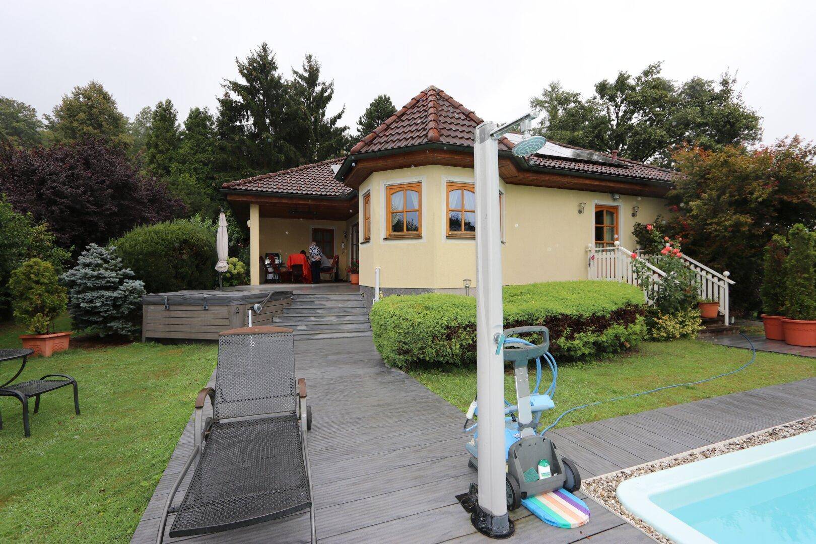 Poolbereich mit Liegestuhl und Außendusche, umgeben von grünem Rasen und dem Haus.