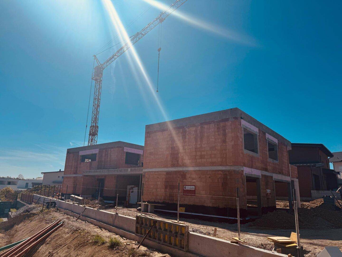 Baustelle mit zwei im Bau befindlichen Häusern und einem Kran unter strahlend blauem Himmel.
