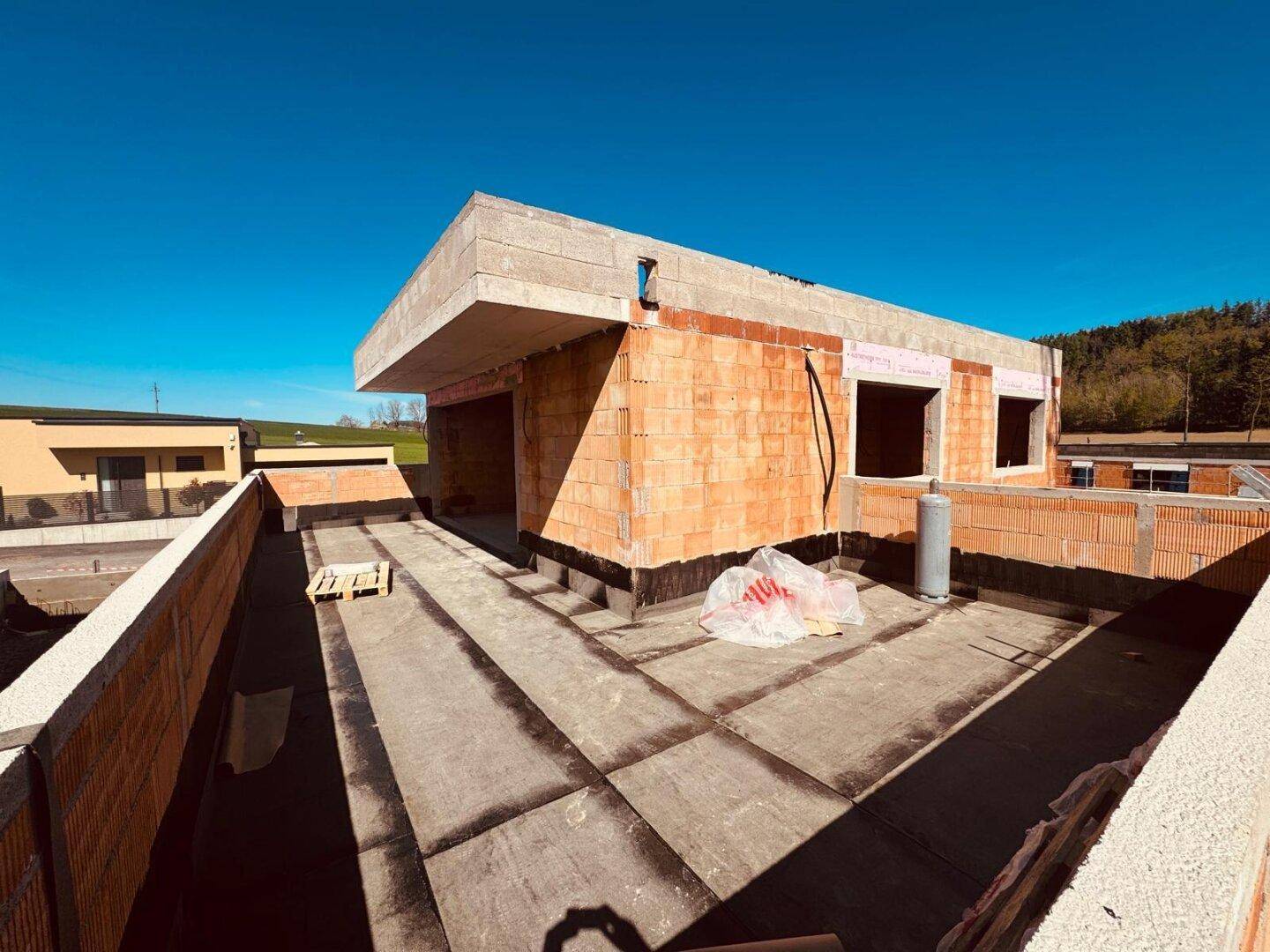 Blick von einem Flachdach eines im Bau befindlichen Hauses mit umliegender Landschaft.