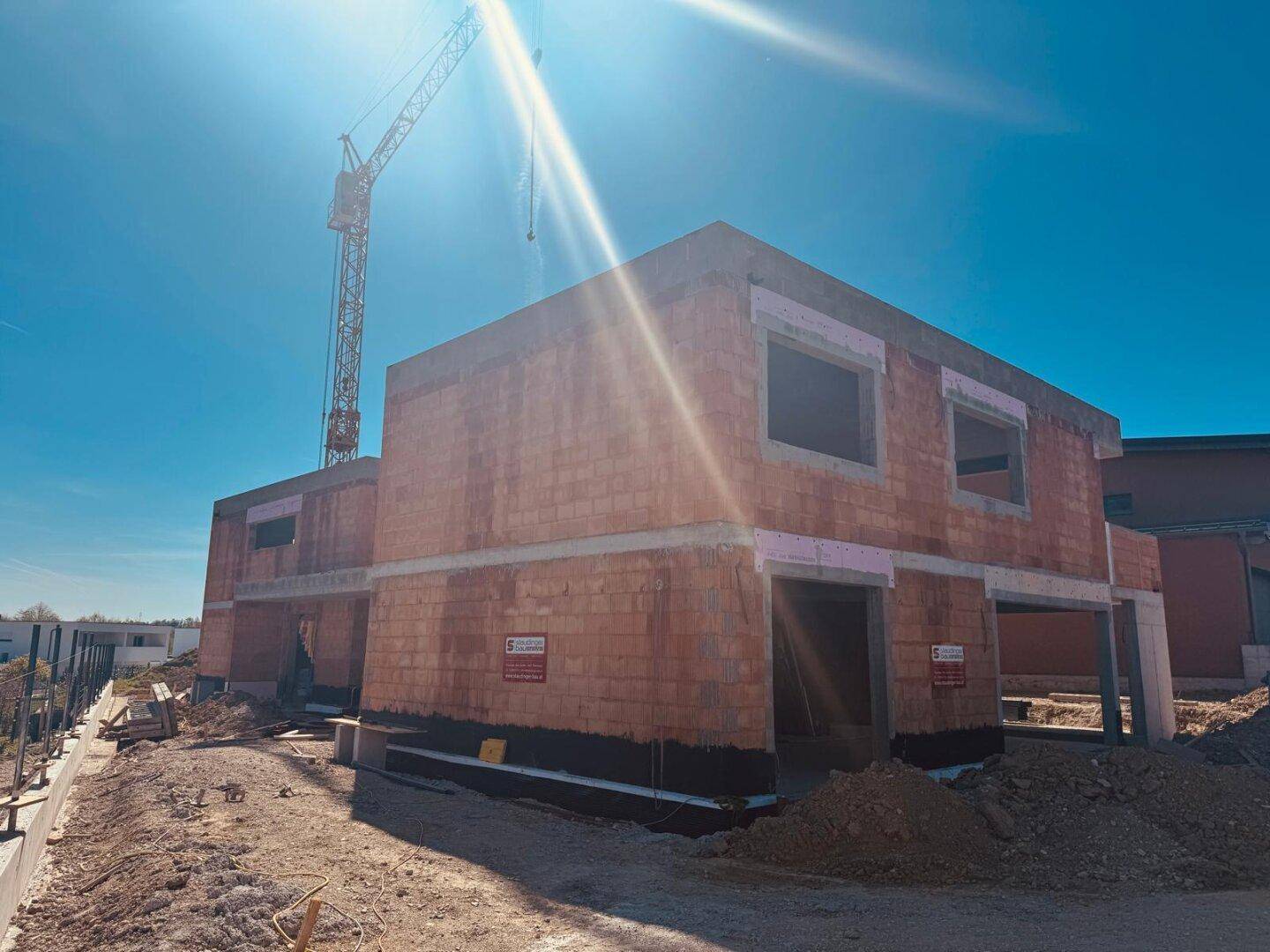 Baustelle mit einem im Bau befindlichen Haus und einem Kran an einem sonnigen Tag.