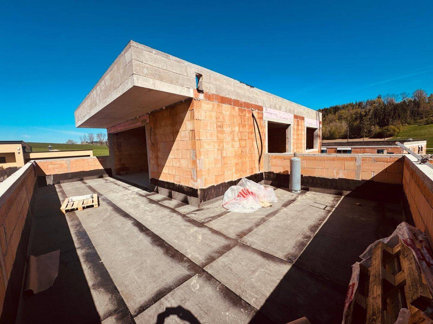 Flachdach eines im Bau befindlichen Hauses mit Blick auf die grüne Hügellandschaft.
