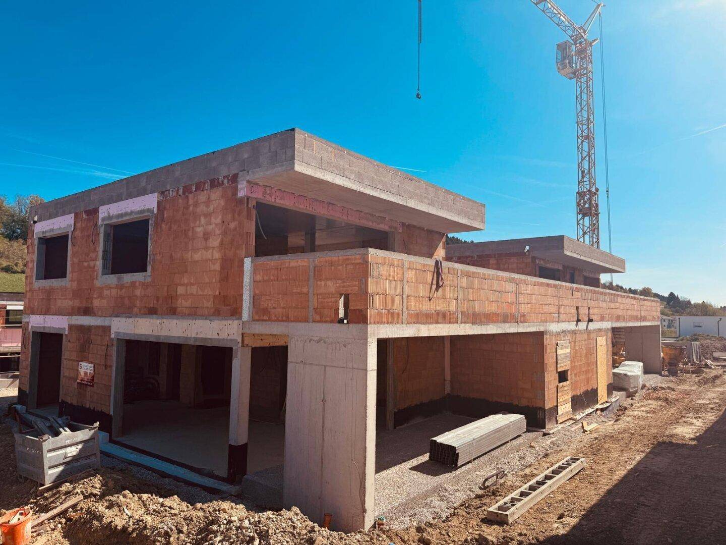 Zwei im Bau befindliche Häuser mit Ziegelmauerwerk und Betonstrukturen an einem sonnigen Tag.