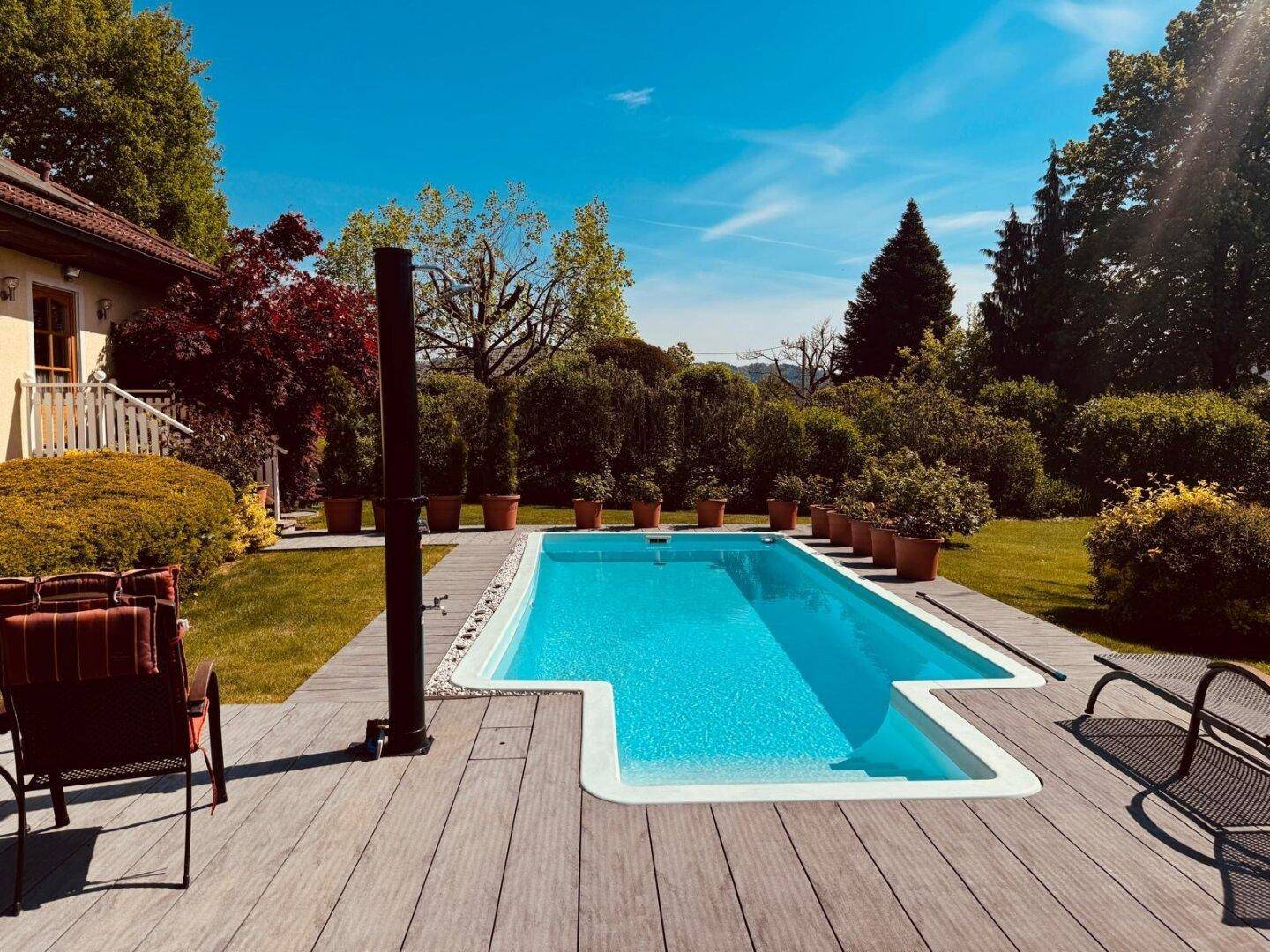 Erfrischender Poolbereich mit Holzdeck und Liegestühlen, umgeben von üppigem Grün.