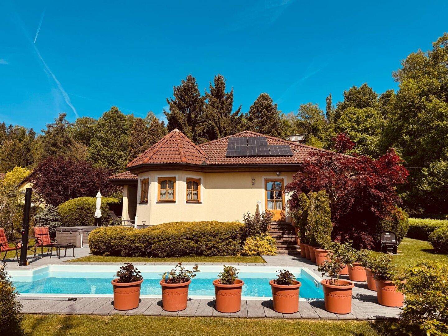 Sonnige Gartenterrasse mit erfrischendem Pool und blühenden Pflanzen rund um das Haus.