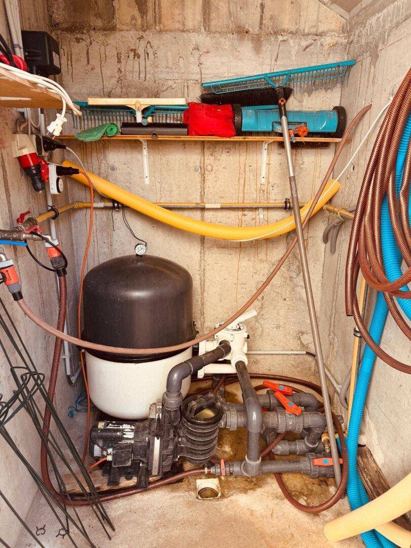 Technikraum mit Wasserpumpe, Rohren und Gartengeräten für die Bewässerung.