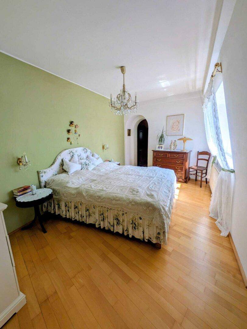 Helles Schlafzimmer mit Holzboden, einer grünen Akzentwand und einem eleganten Kronleuchter.