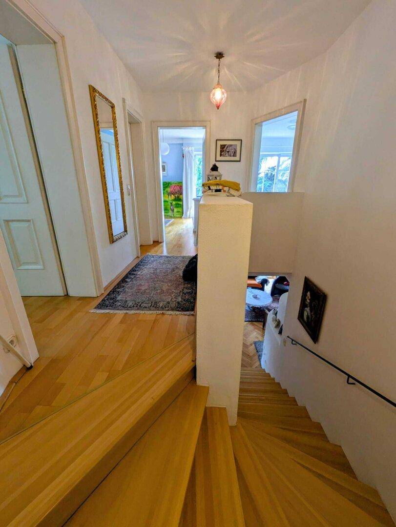 Heller Flur mit Holztreppe und Zugang zu weiteren Räumen, geschmückt mit einem Spiegel.