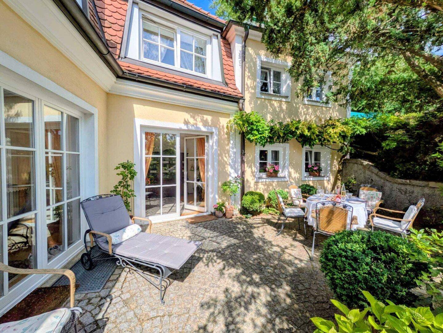 Geräumige gepflasterte Terrasse mit Essbereich und Liegestuhl, umgeben von einem gepflegten Garten.