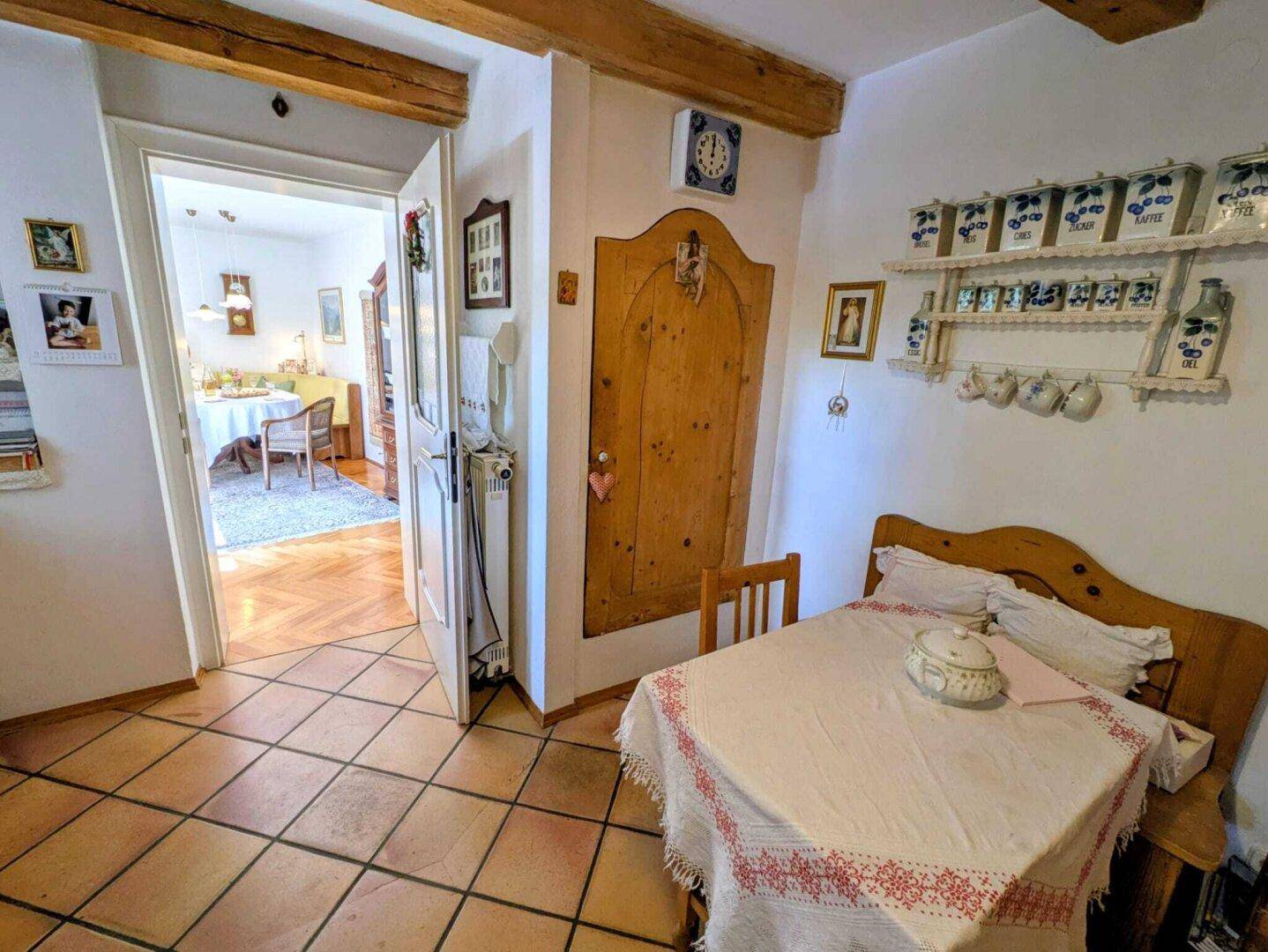 Rustikaler Essbereich mit Terrakottafliesen und Holzbalken, angrenzend an ein Zimmer mit Parkettboden.