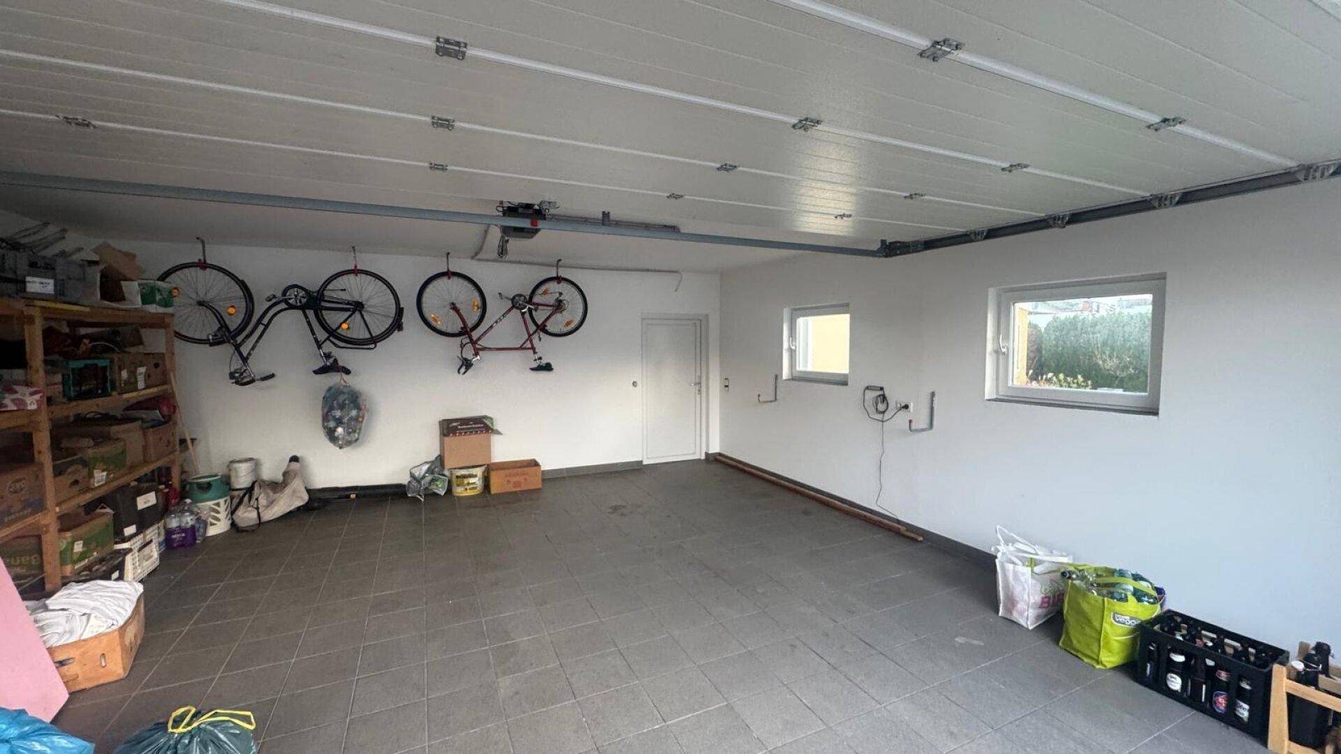 Geräumige Garage mit Fliesenboden, Fenstern und praktischen Fahrradaufhängungen an der Wand.