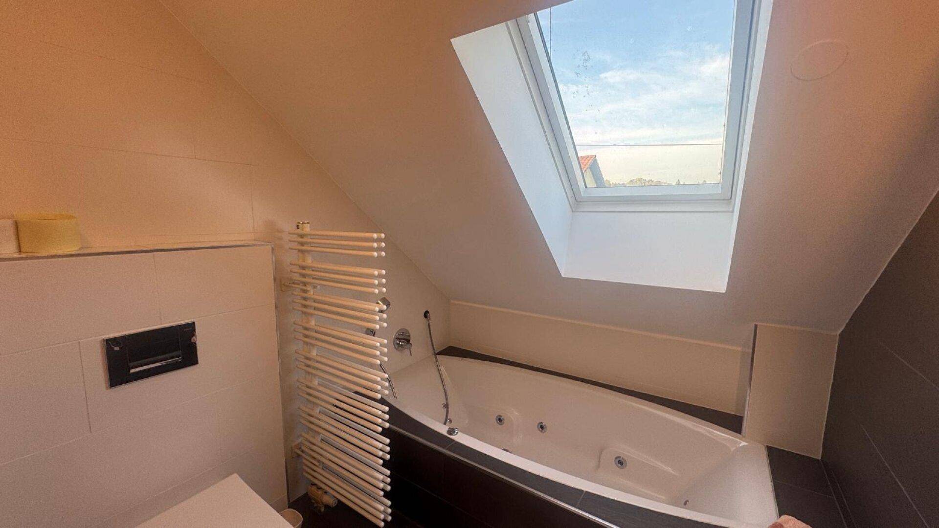 Dachgeschoss-Badezimmer mit Whirlpool-Badewanne, Dachfenster und beheiztem Handtuchhalter.