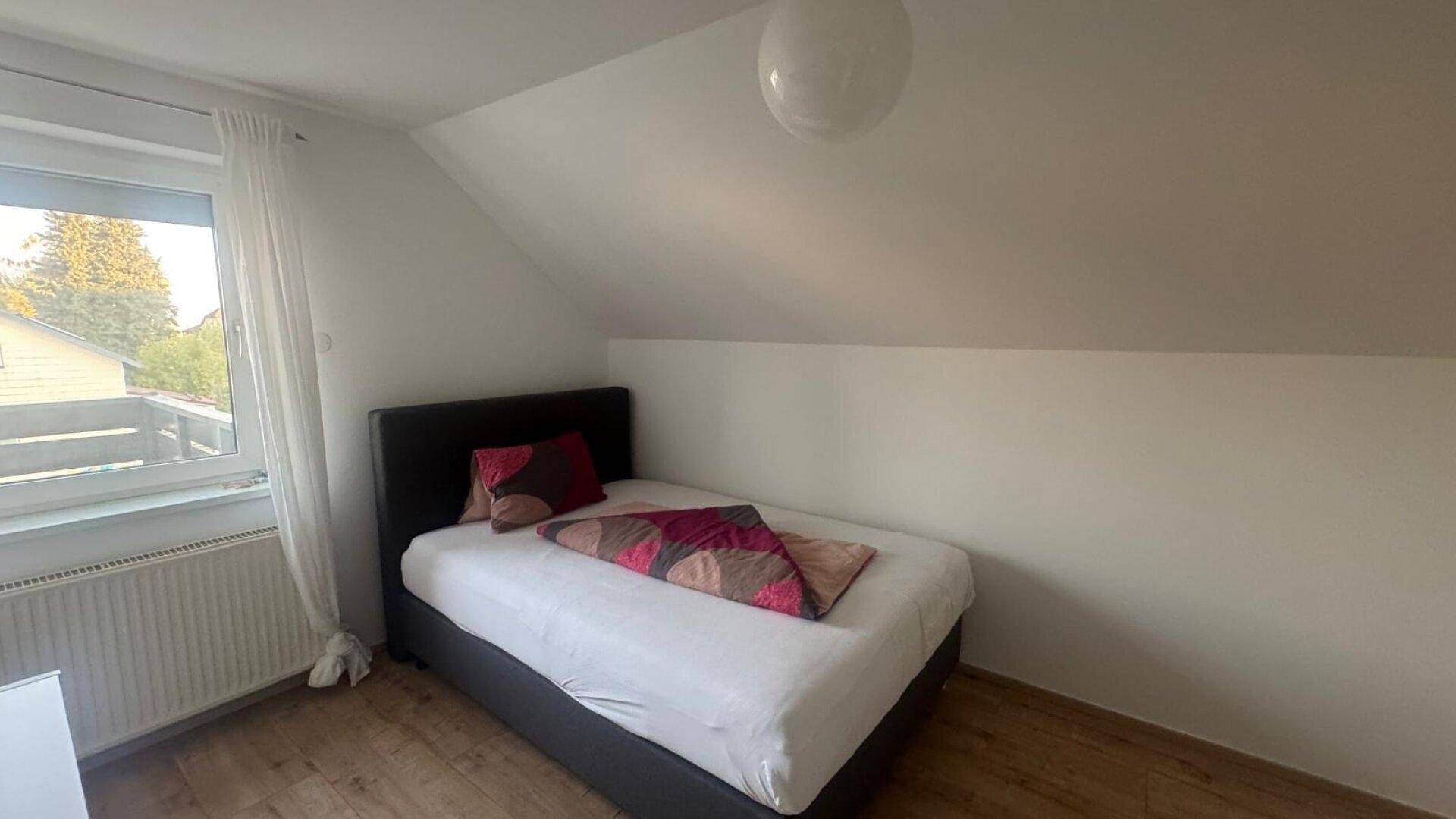 Gemütliches Schlafzimmer im Dachgeschoss mit Einzelbett, Holzboden und Fenster für Tageslicht.