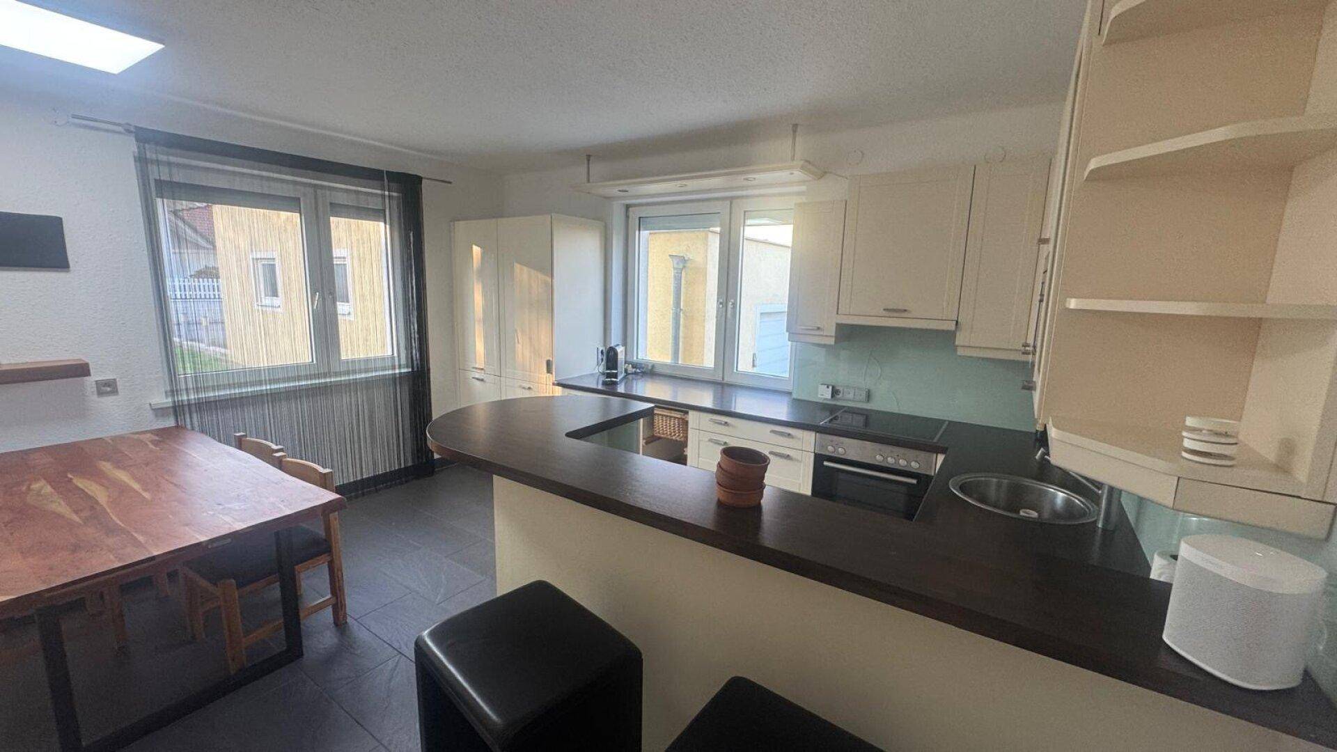 Offene Küche mit Bartheke, cremefarbenen Schränken und Essbereich am Fenster.