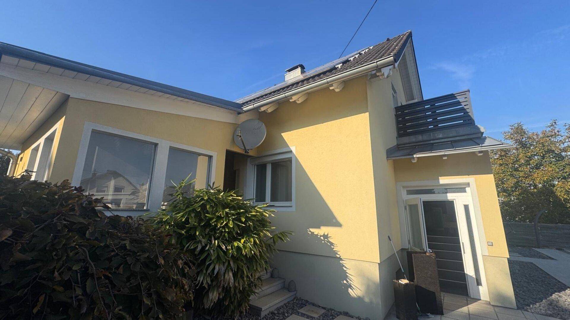 Eingangsbereich des Hauses mit Satellitenschüssel, gepflegter Bepflanzung und Zugang zum Gebäude.