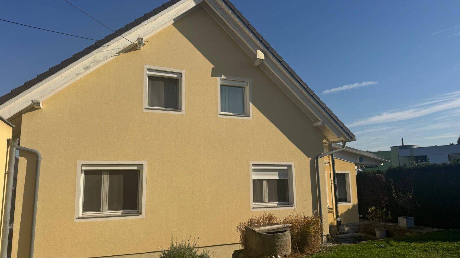 Seitenansicht des gelben Einfamilienhauses mit mehreren Fenstern, Rollläden und sauberer Fassade.