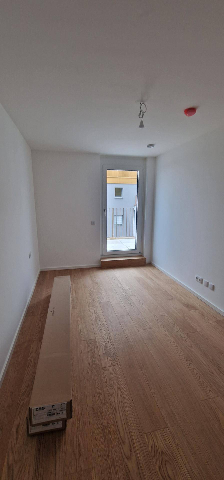 Leerer Raum mit Holzboden und Zugang zu einem kleinen Balkon, ideal für ein Schlafzimmer oder Büro.