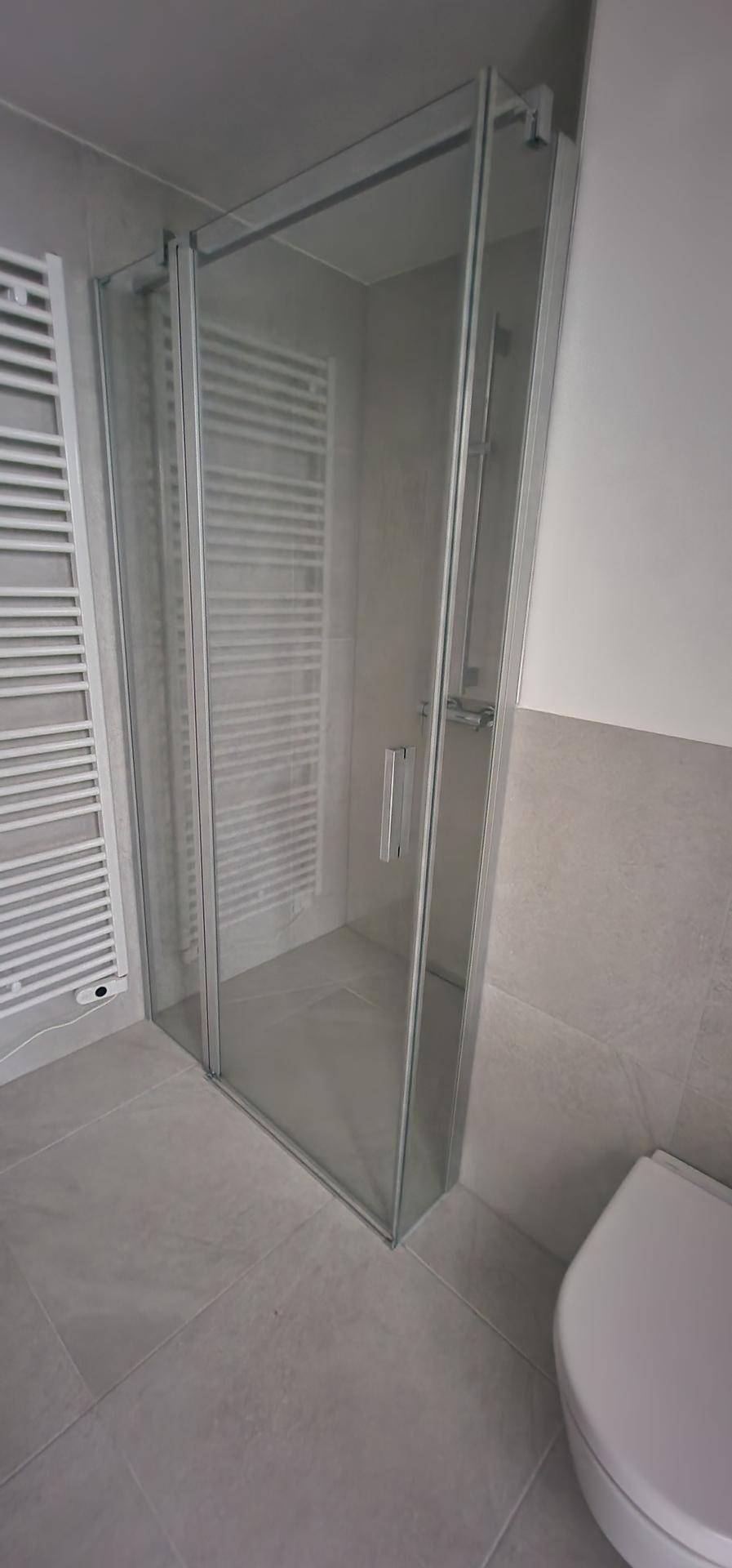 Modernes Badezimmer mit Duschkabine, beheiztem Handtuchhalter und grauen Wand- und Bodenfliesen.