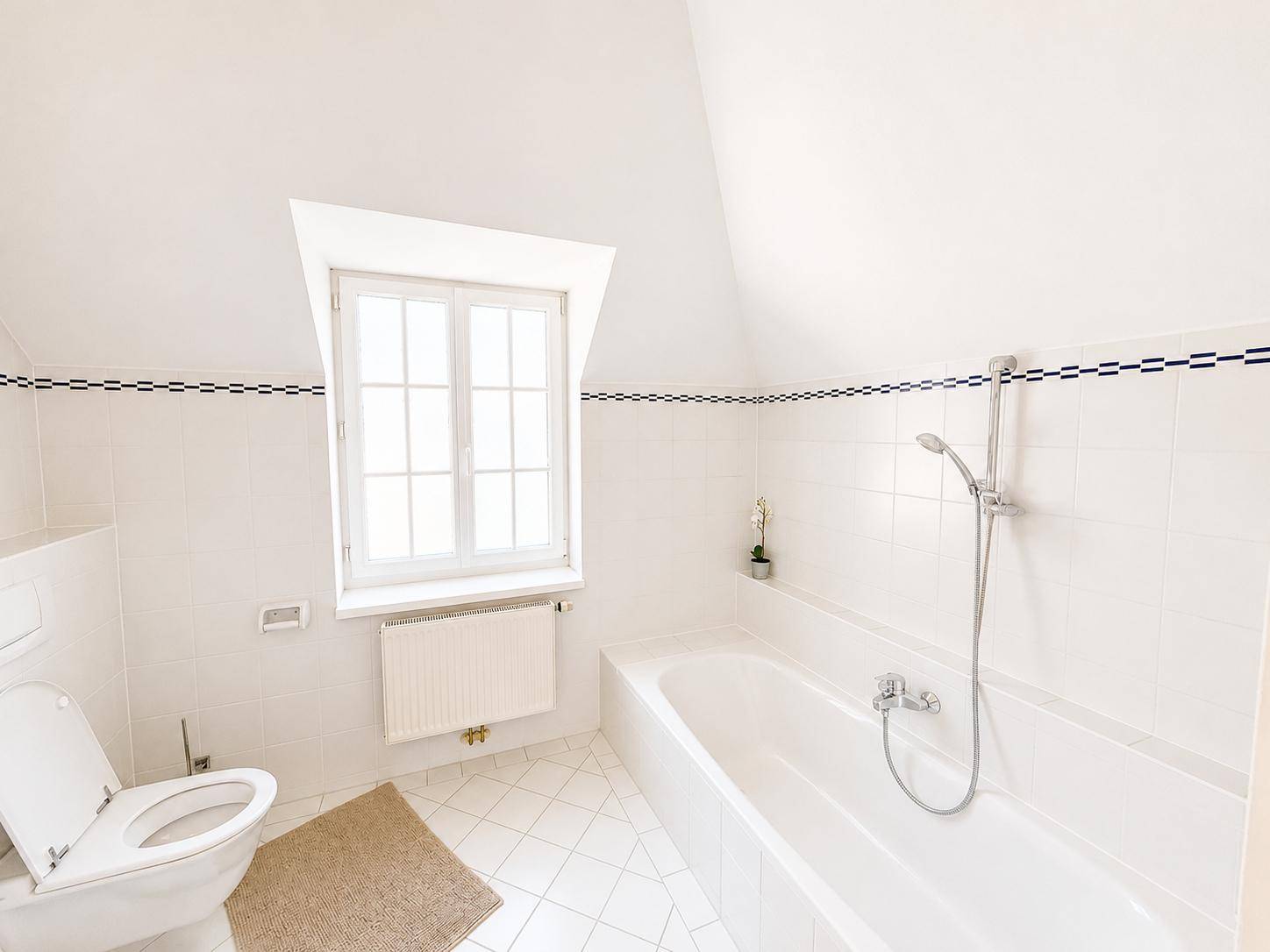 Helles Badezimmer mit Badewanne, WC, weißen Fliesen und Dachfenster.