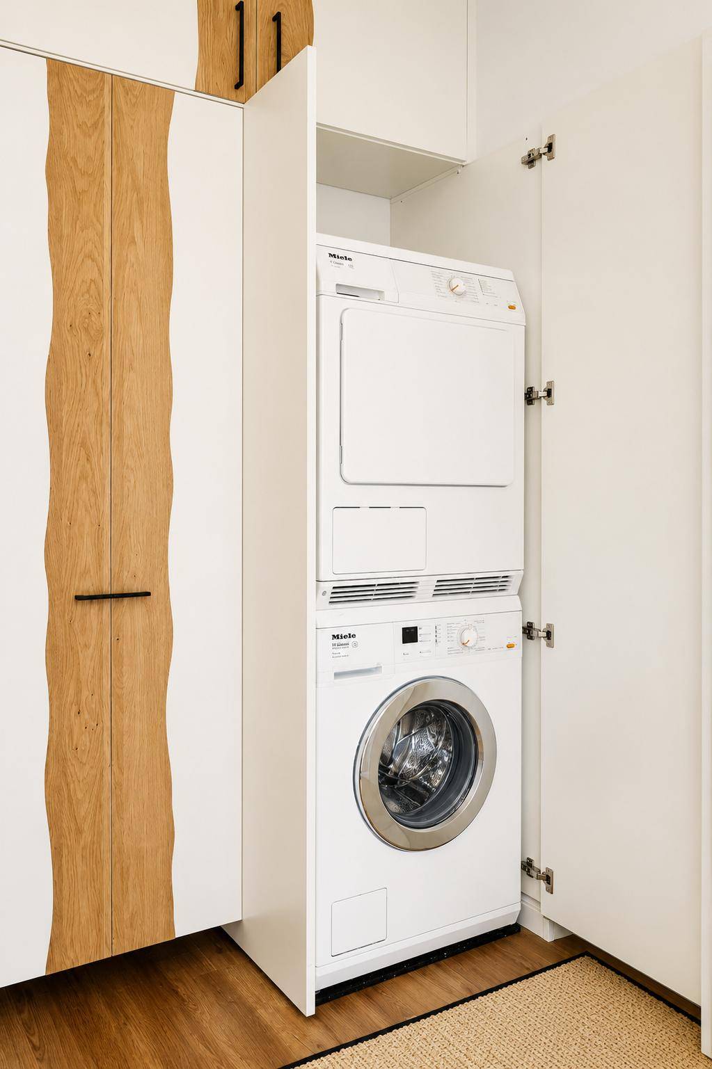 Praktischer Hauswirtschaftsraum mit integrierter Waschmaschine und Trockner von Miele in maßgefertigten Schränken.