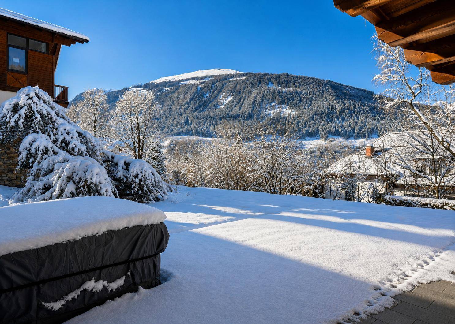 Sonniger Gartenbereich mit Schnee bedeckt und weitem Blick auf die verschneiten Berge.