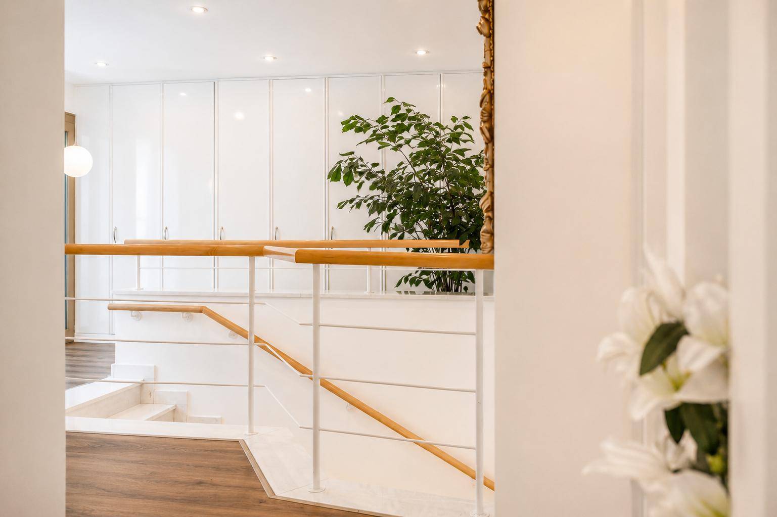 Heller Flur mit moderner Treppe, Holzgeländer und weißen Einbauschränken.