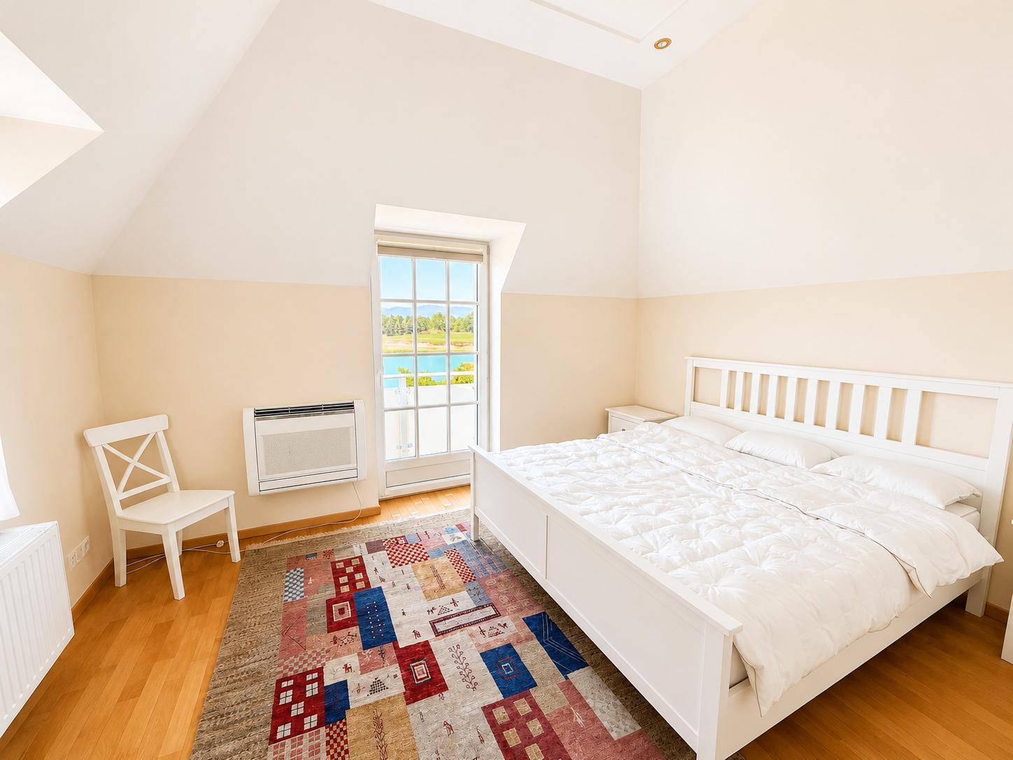 Helles Schlafzimmer im Dachgeschoss mit Seeblick, Holzboden und modernem Teppich.