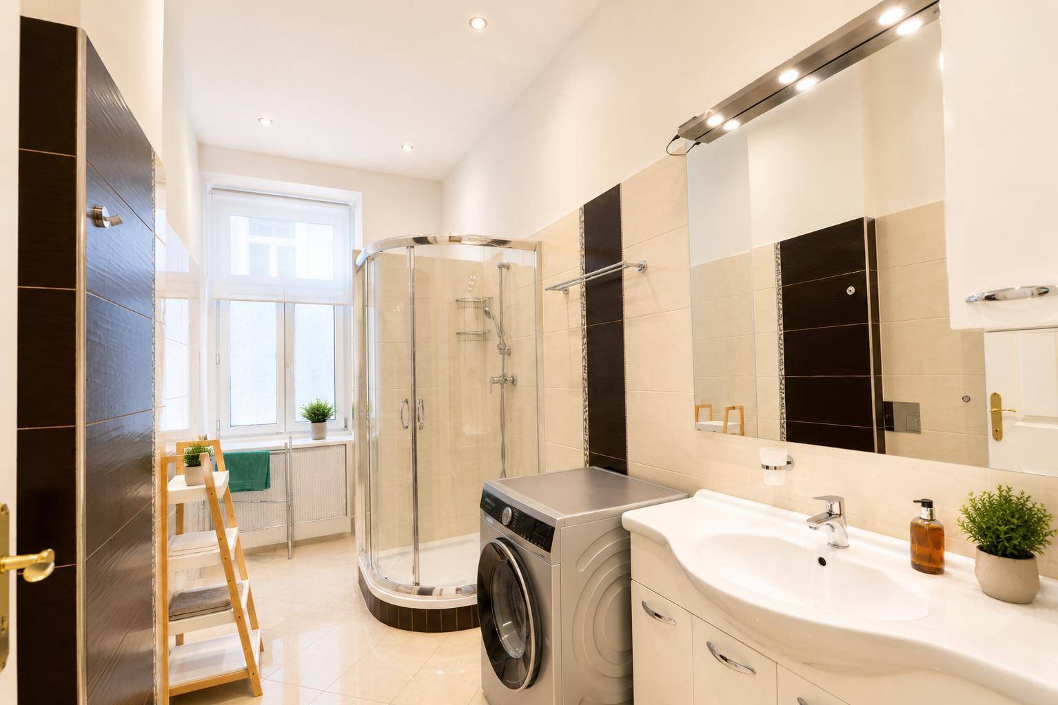 Modernes Badezimmer mit Duschkabine, Waschbecken und Waschmaschine, hell durch Fenster.