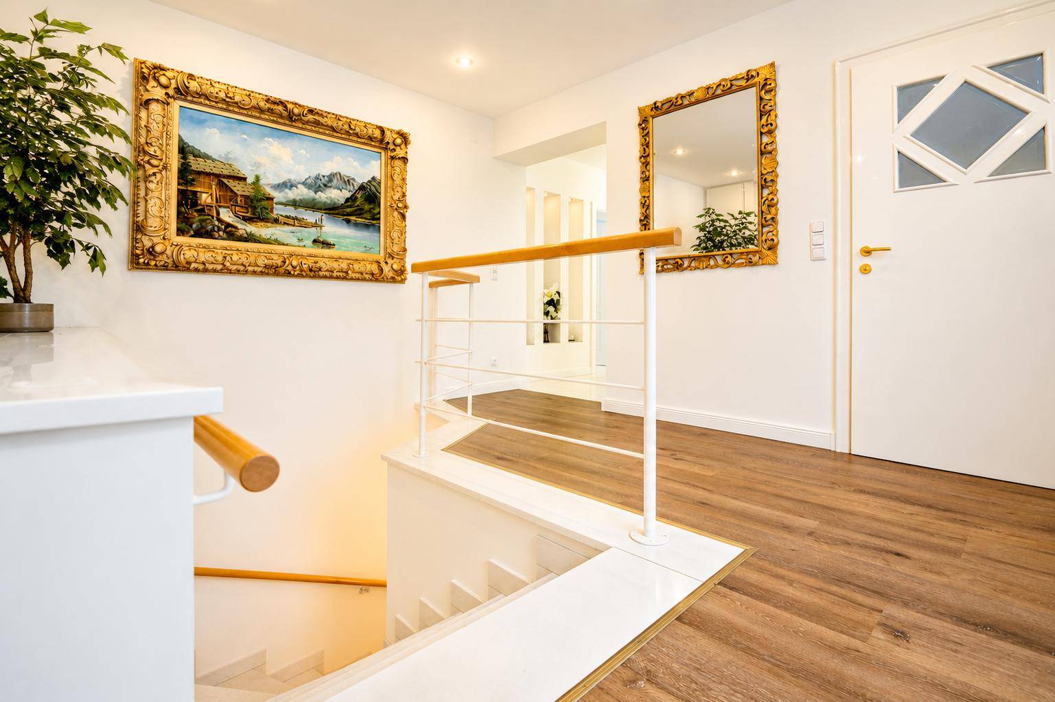 Heller Flur mit Holztreppe, modernem Geländer und dekorativen Gemälden an den Wänden.
