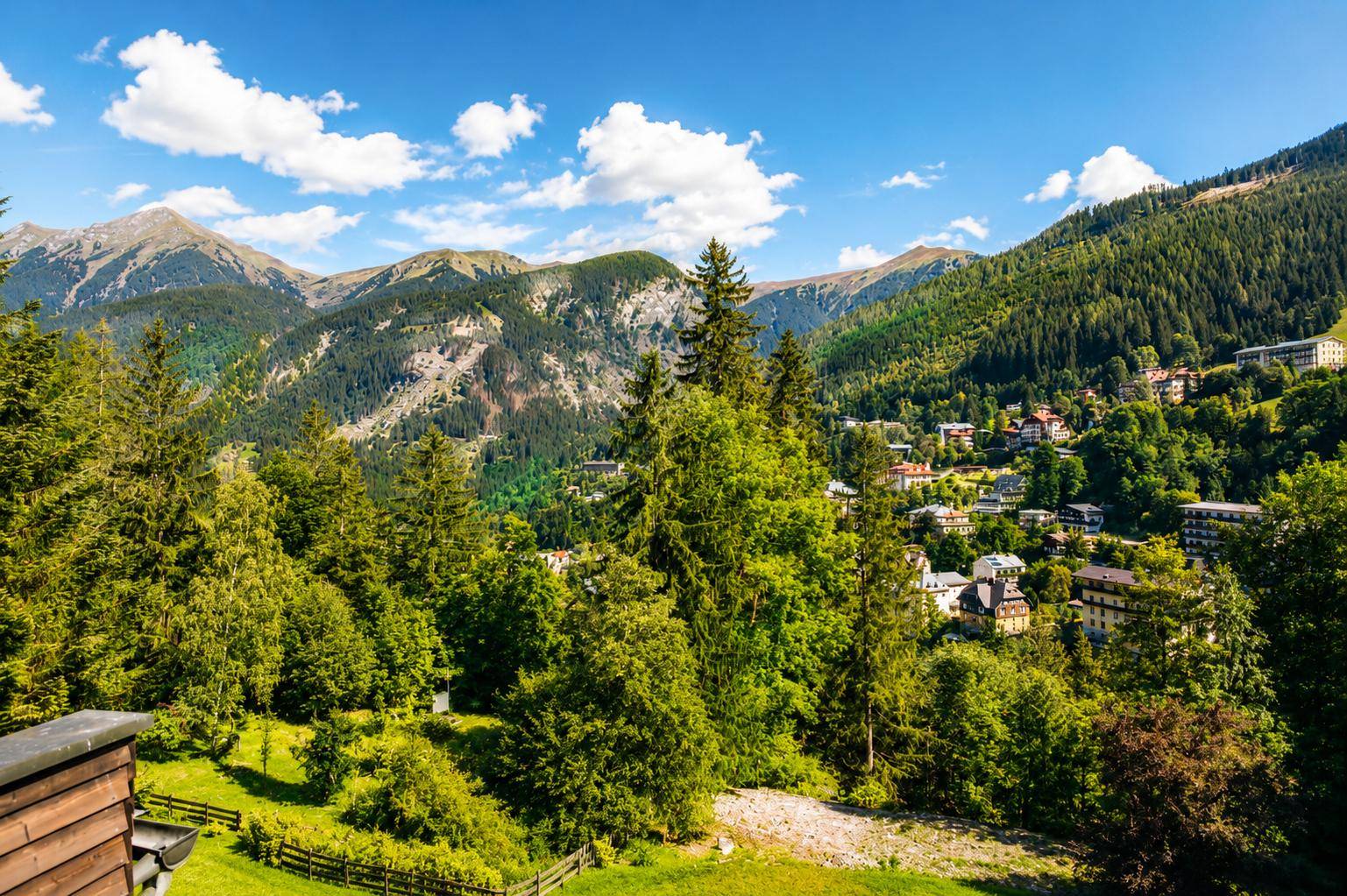 Malerischer Bergblick mit grünen Wäldern und einem Dorf in der Ferne unter blauem Himmel.