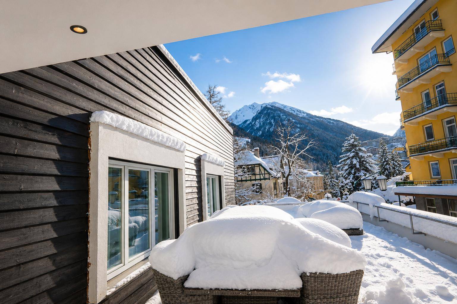 Verschneite Terrasse mit Sitzgelegenheiten und Blick auf die winterliche Berglandschaft.