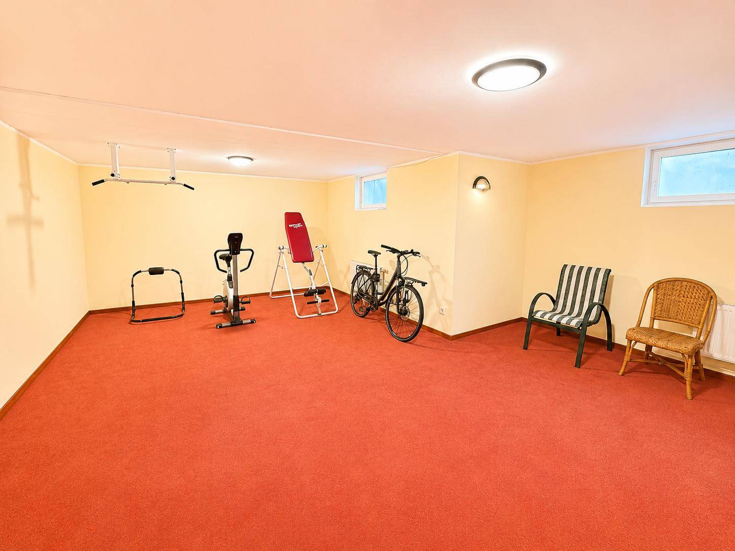 Geräumiger Fitnessraum im Keller mit verschiedenen Trainingsgeräten und Teppichboden.