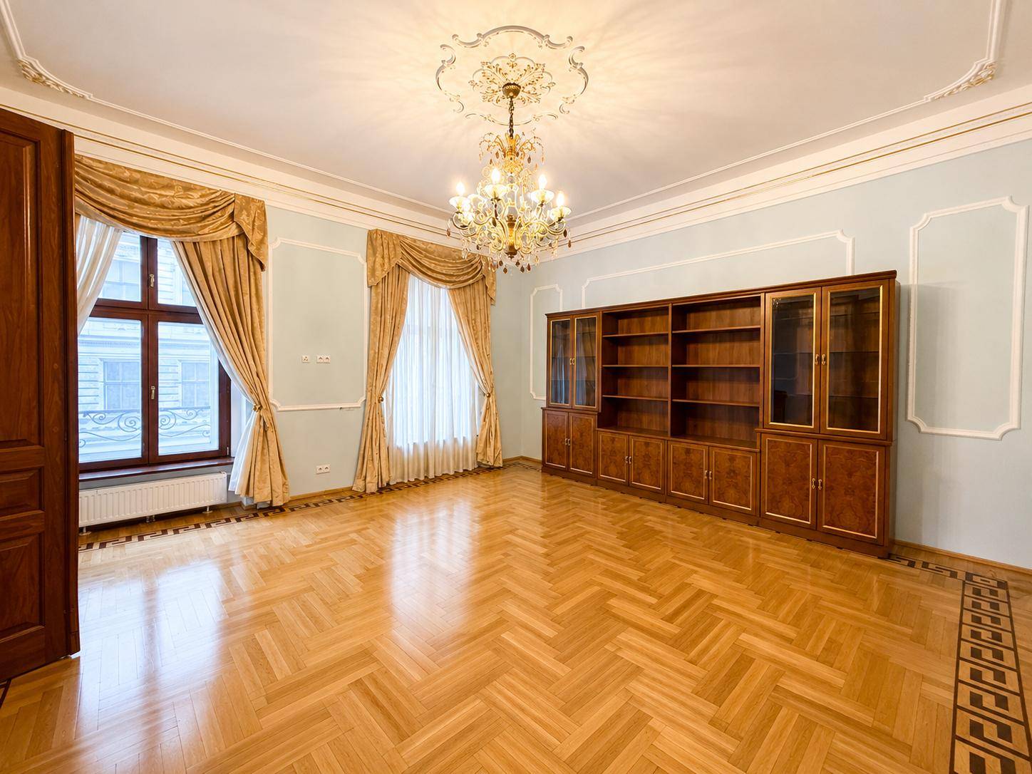 Elegantes Zimmer mit Parkettboden, großem Einbaubücherregal und einem prunkvollen Kronleuchter.