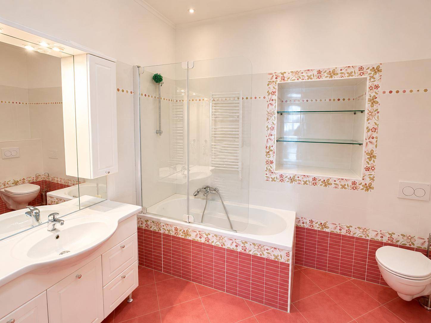 Helles Badezimmer mit Badewanne, Duschabtrennung, WC und floralen Dekorelementen an den Wänden.