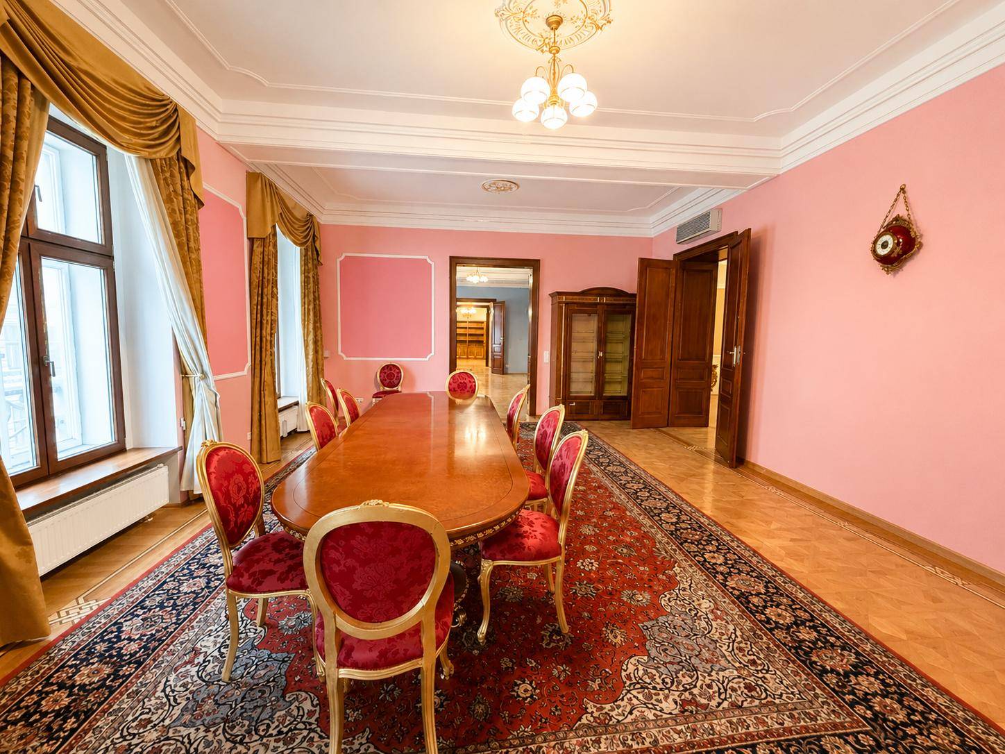 Großes Esszimmer mit langem Holztisch, roten Stühlen und Parkettboden auf einem orientalischen Teppich.