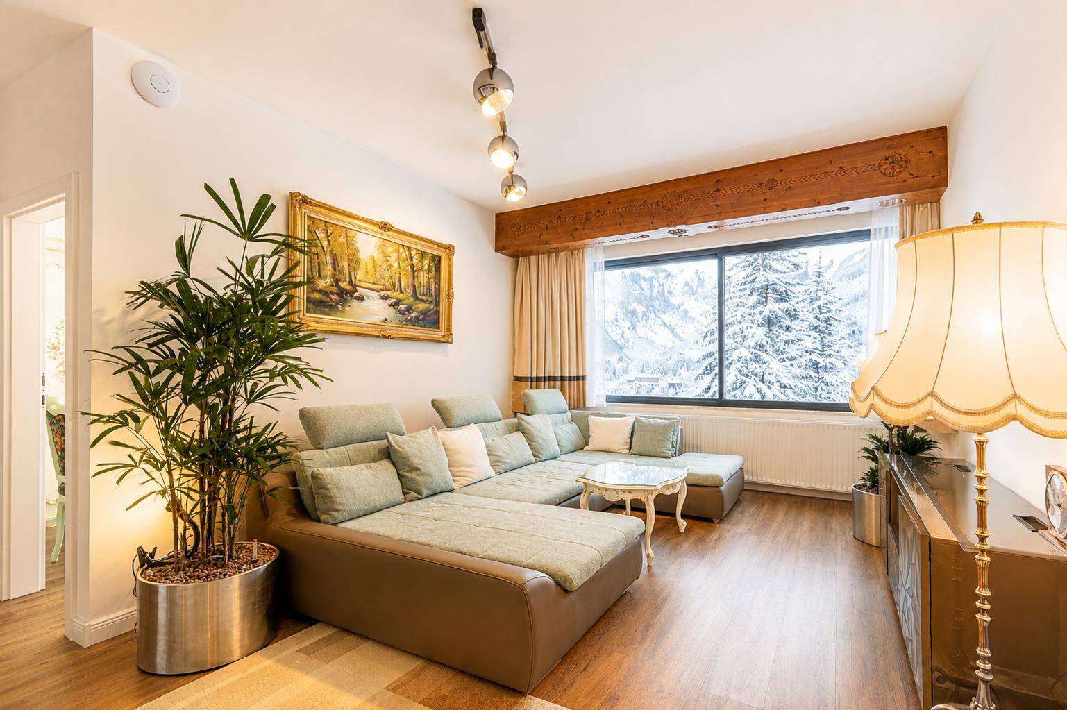 Gemütliches Wohnzimmer mit großem Ecksofa, Holzbalken und Blick auf verschneite Berge.