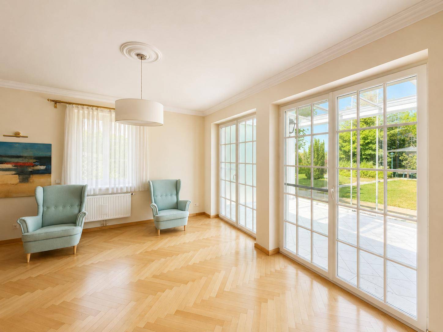 Helles Wohnzimmer mit Fischgrätparkett, großen Fenstern und Blick in den Garten.