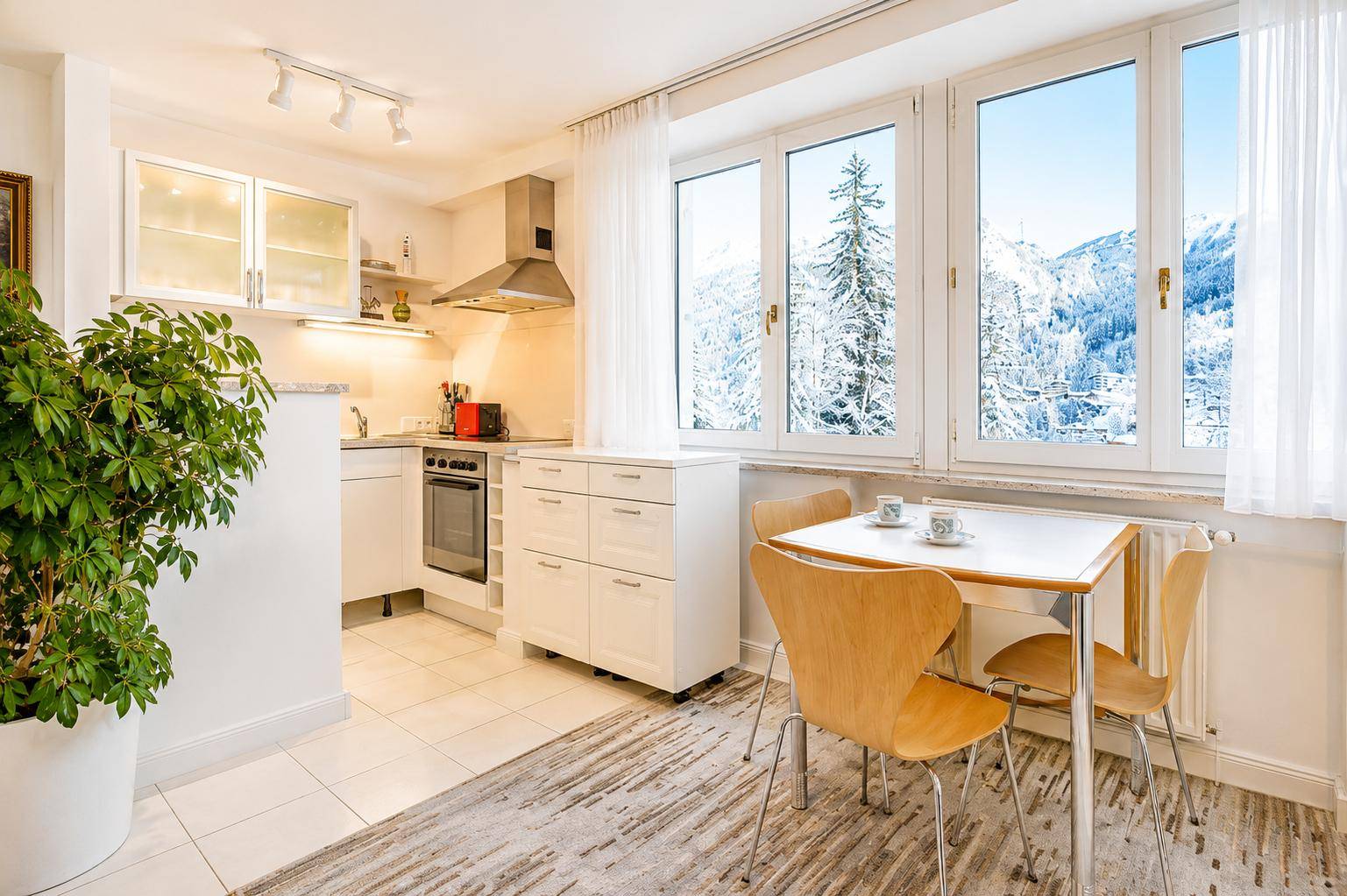 Helle Küche mit weißen Schränken, Esstisch und Blick auf die verschneite Berglandschaft.