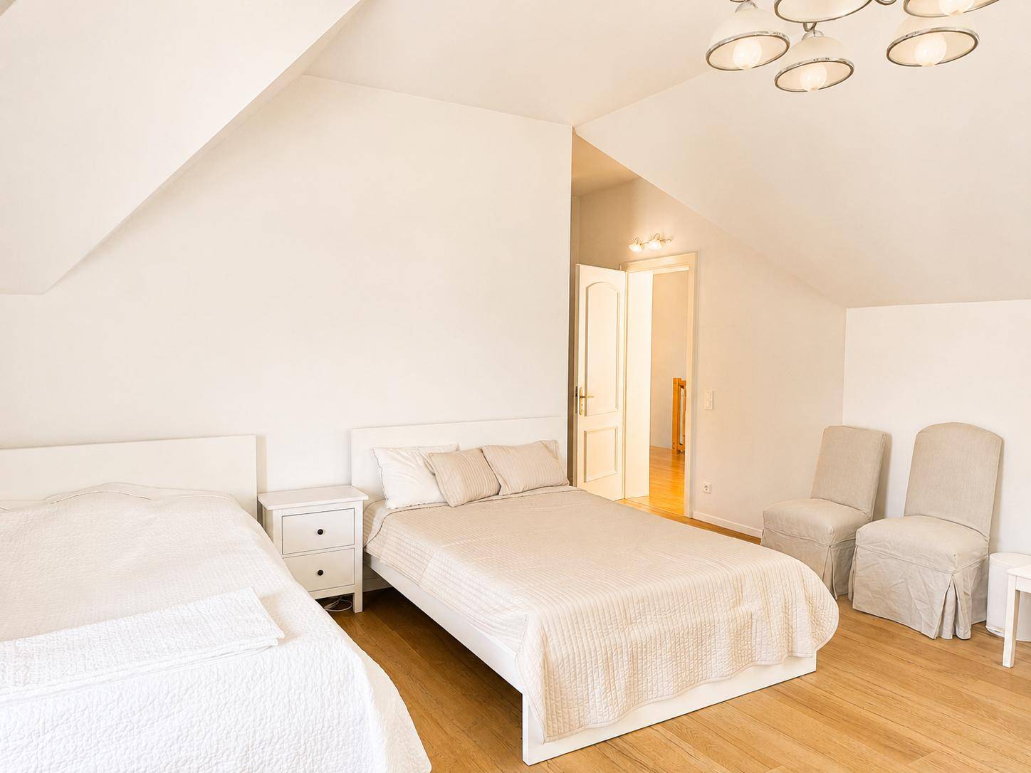 Geräumiges Schlafzimmer im Dachgeschoss mit zwei Betten, Holzboden und Zugang zum Flur.