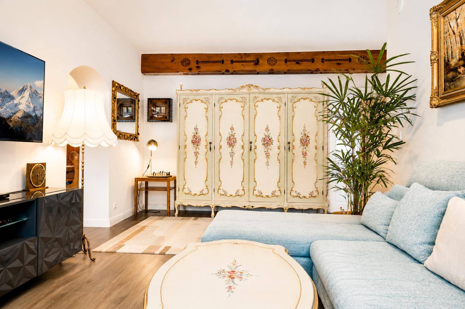 Gemütliches Wohnzimmer mit hellblauer Couch, antikem Schrank und Holzbalken an der Decke.